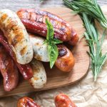 Cooked sausages on a wooden serving board, garnished with herbs.