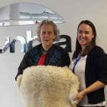 Dr Temple Grandin, left, and Dr Sally Hill, right, stand holding a lambs fleece between the two of them. They are pictured standing in front of the Dunbia logo on a wall.