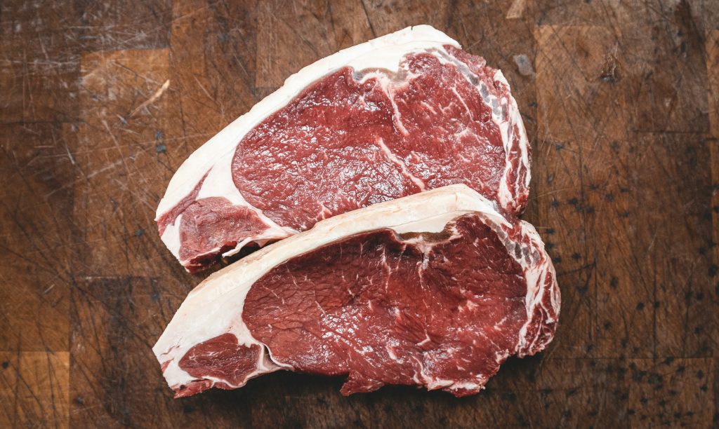 Two cuts of beef are in the centre of the frame, lying in the middle of a wooden board.